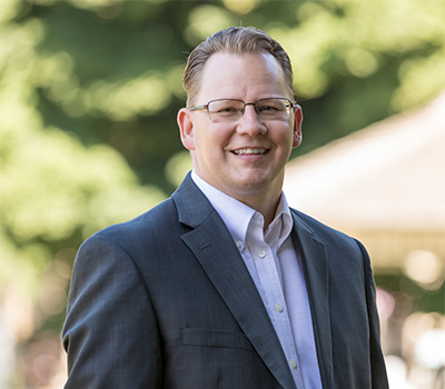 Superintendent Chris Reykdal outside with trees behind him.