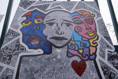 A colorful abstract artwork featuring two stylized faces with vibrant colors and intricate patterns. The background is filled with detailed black and white designs, including text in French.