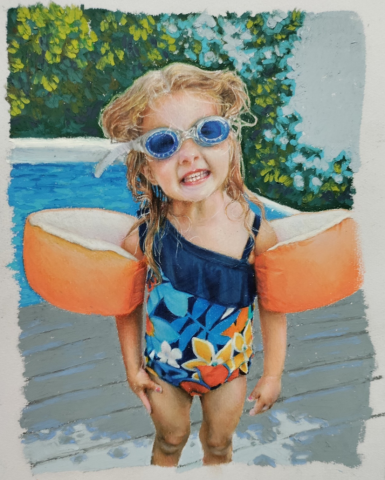 A young child standing outdoors near a pool, wearing a colorful swimsuit with floral patterns and orange floaties on both arms. 