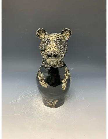 The artwork features a black ceramic vase with a bear's head as the lid. The bear's head is detailed with textured fur and expressive eyes, while the body of the vase showcases delicate golden floral patterns.