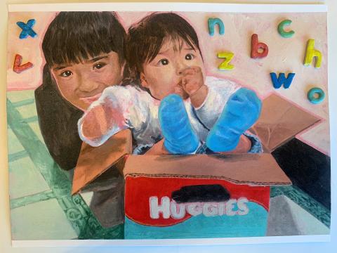 The artwork features two children sitting inside a cardboard box labeled "Huggies." The child in front is wearing blue socks and white clothing, while the child behind has darker hair. The background includes a green-tiled floor and colorful magnetic letters scattered around.