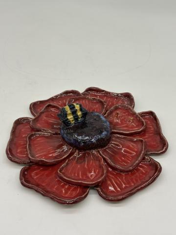 Clay flower, with red petals and a dark center. Sitting on it is a tank, but it is small and the same relative size as a bee, and has yellow and black stripes on it.