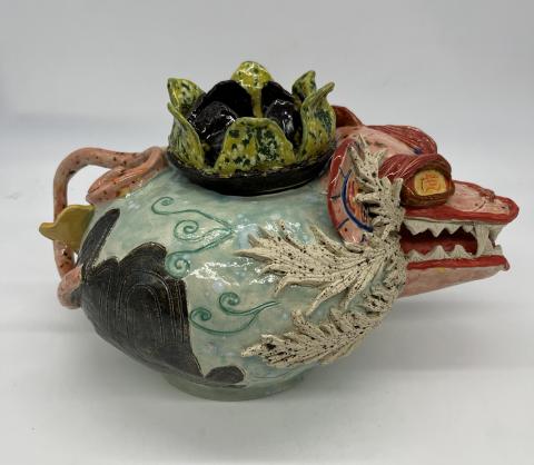 The image shows a colorful ceramic teapot adorned with various animals, including a tiger, a moth, and a bird.
