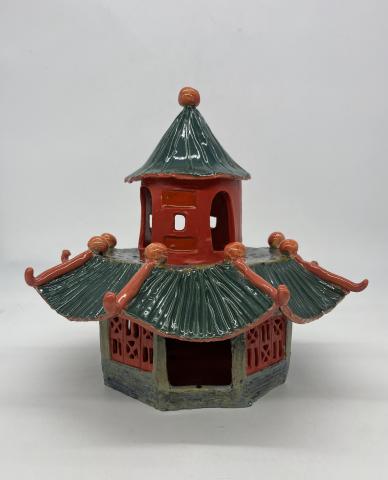 A two story, maroon and emerald green temple, with cut outs and textured walls/roof.