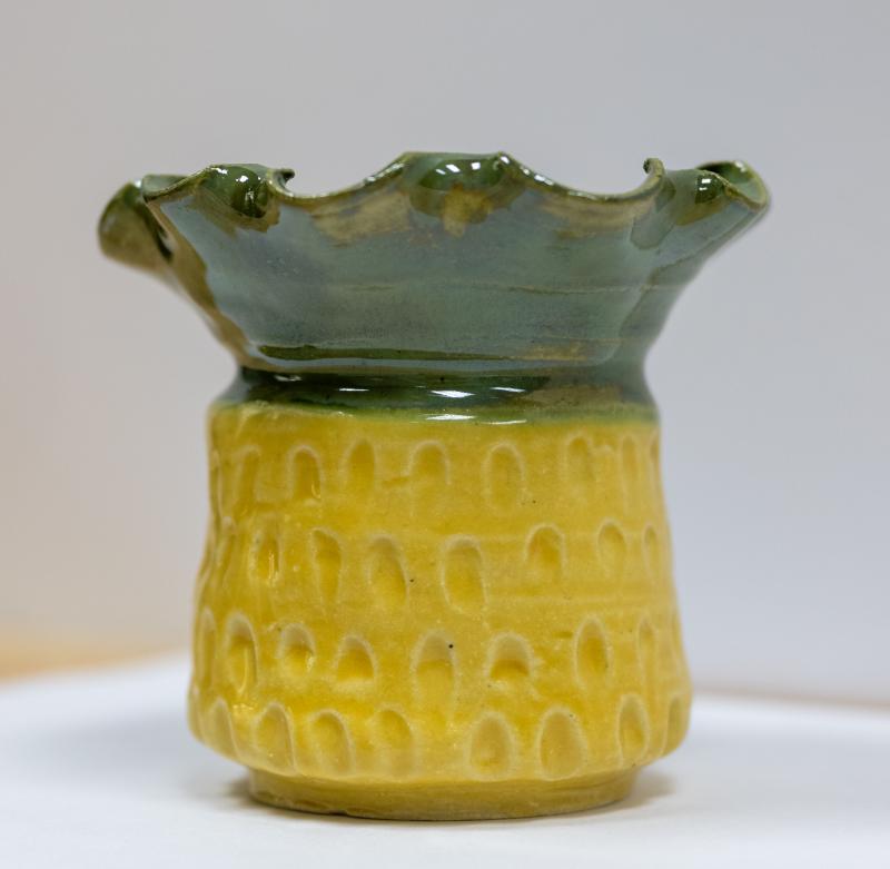 A ceramic vase with a textured yellow base and a green, wavy rim. 
