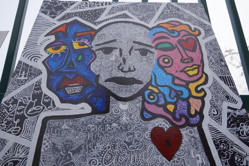 A colorful abstract artwork featuring two stylized faces with vibrant colors and intricate patterns. The background is filled with detailed black and white designs, including text in French.