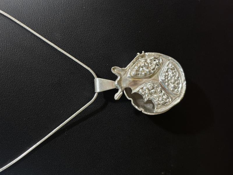 A silver pendant in the shape of a pomegranate.