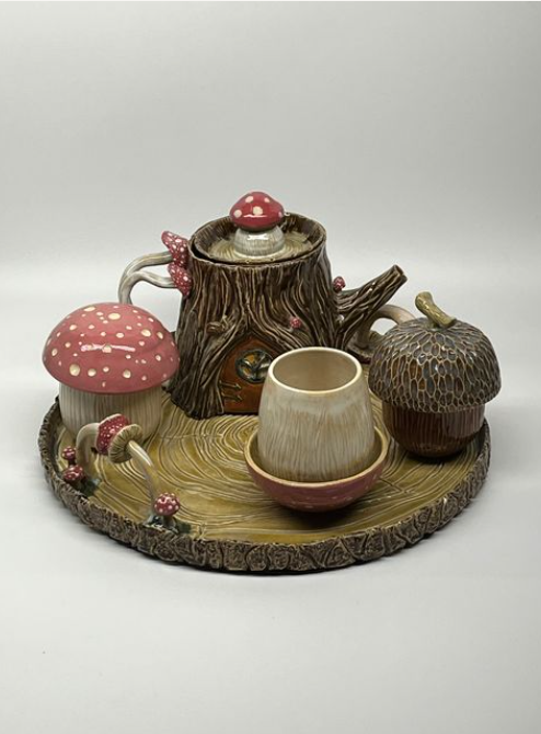 A clay composition of a pot of tea, with a cup and mushrooms on a tree stump