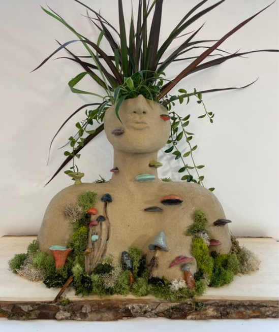A mixed media creation of a woman's head and upperbody being consumed by an overgrowth of  foliage and mushrooms