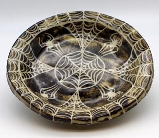 a clay ceramic creation of a brown black bowl with abradial spider web design