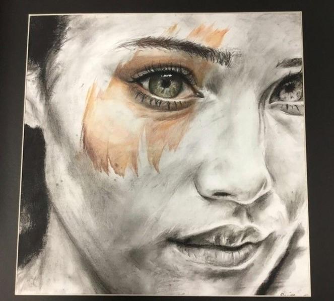 A charcoal drawing of a girl's face in grey monotones with watercolor used on the eye to bring the image to life. 