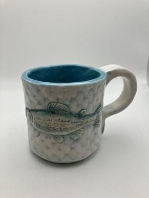 A ceramic mug with blue and white hues with a trout visible and the tail as part of the handle