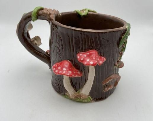 A brown ceramic mug with red mushrooms and vine circling the handle