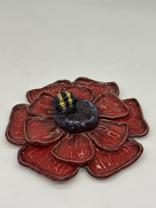 Clay flower, with red petals and a dark center. Sitting on it is a tank, but it is small and the same relative size as a bee, and has yellow and black stripes on it.