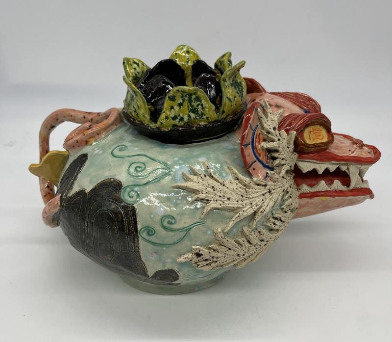 The image shows a colorful ceramic teapot adorned with various animals, including a tiger, a moth, and a bird.