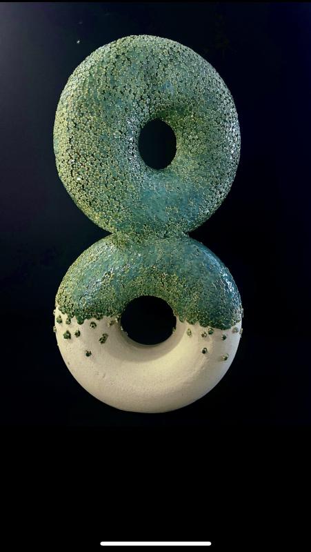 Two wheel-thrown ceramic vessels joined into an infinity form, featuring delicate, hand-built flowers with green glaze flowing over a contrasting raw clay surface.