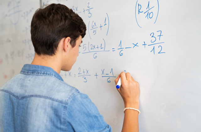 Student at a white board working on a math problem.