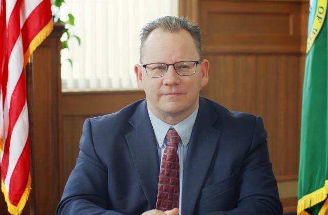 Superintendent Reykdal sitting at a desk Washington State and United States flags behind him.