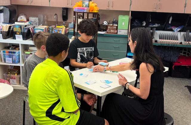 A group of students and their teacher sit at a desk doing math.