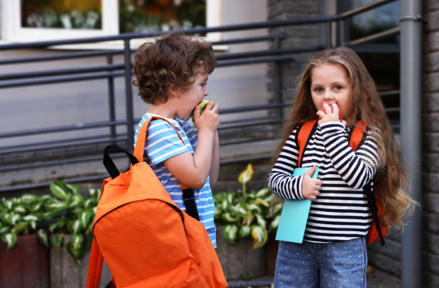 two kids eating apples wearing backpacks