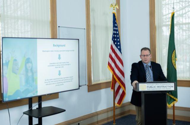 Superintendent Reykdal behind a podium next to a T.V. screen 