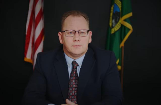 State Superintendent sitting at desk with the American and Washington state flags in the background