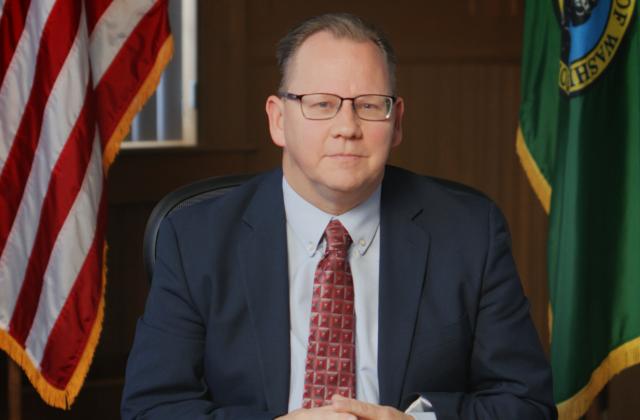 Superintendent Reykdal sitting at a desk with the US and Washington state flags behind him